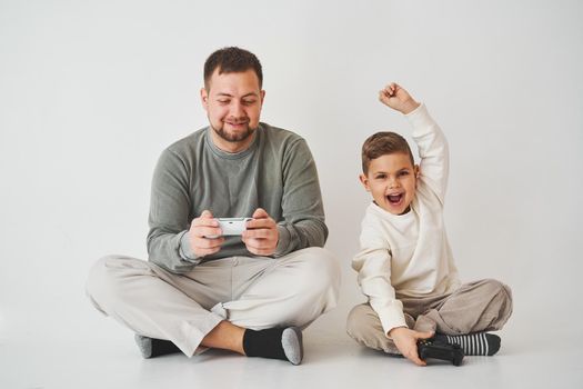 Son won father in game on console. Happy child with gamepad raises his hands up and rejoices in the victory in the game