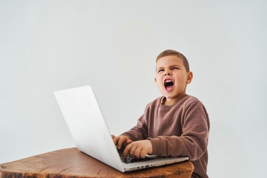 Emotional child with laptop shout. Gambling addiction. Handsome child gamer play online games on laptop on white background