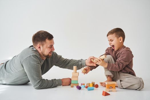 Dad and son smiling, having fun and playing colored bricks toy on white background. Paternity. Caring father with his child