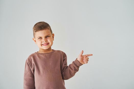 Happy handsome child boy smiling and pointing finger right side. Business advertising for children stores and shops