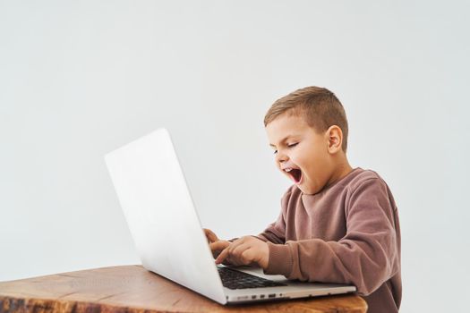 Emotional child play online games on laptop. Gambling addiction. Handsome kid gamer is gaming on laptop on white background