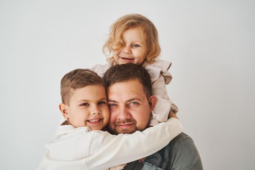 Close-up portrait of father, son and daughter. Happy family hugging and smiling on white background. Paternity. Single father bring up his children