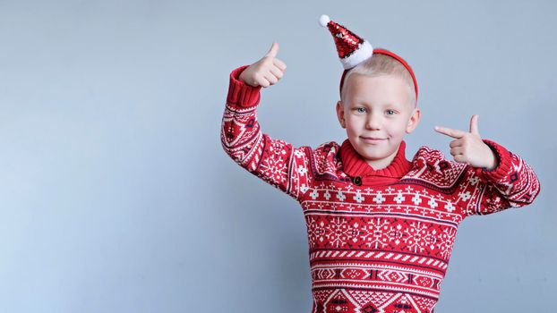 Child in christmas red hat and sweater on gray background. New year and x-mas concept.
