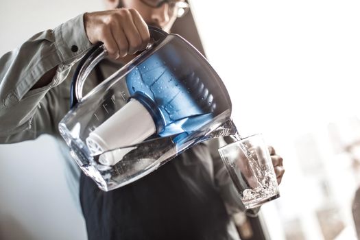 close up. attractive man pouring filtered water into a glass