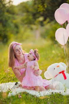 mother and daughter in pink dresses and with pink balloons in nature