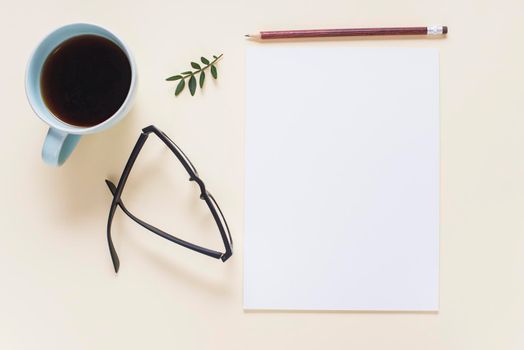 coffee cup eyeglasses twig pencil blank white page beige backdrop