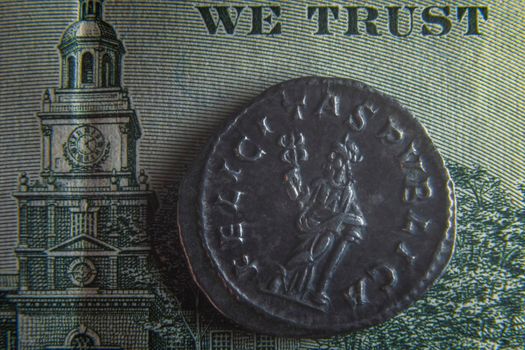 An old Roman coin lies on a 100 dollar bill near the badge with an eagle