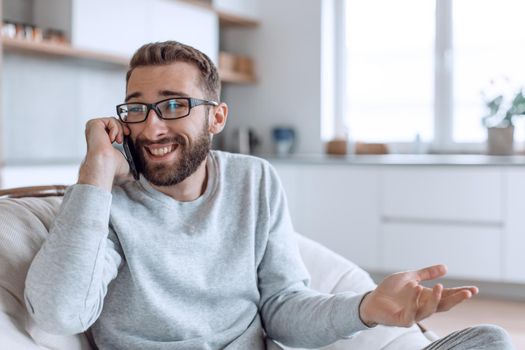 cheerful man talking on a mobile phone sitting in a comfortable chair. photo with copy space