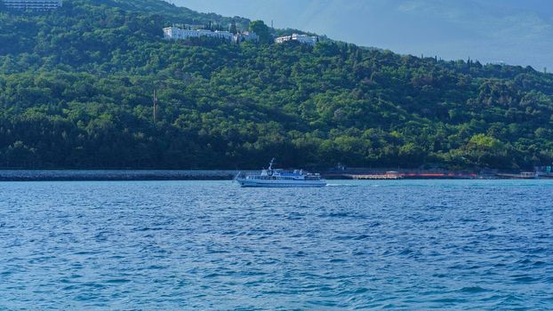 Yalta, Crimea-June 12, 2021: Seascape with a pleasure boat against the backdrop of the coastline.