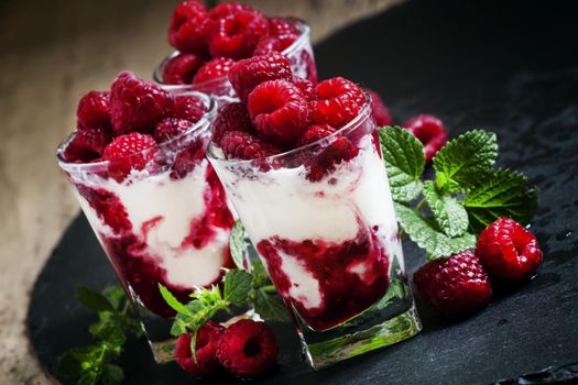 Vanilla ice cream with raspberries and mint dessert served in glasses on dark background, selective focus