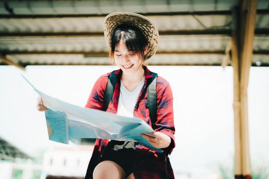 summer, relax, vacation, travel, portrait of a cute Asian girl looking at a map to plan a trip while waiting at the train station