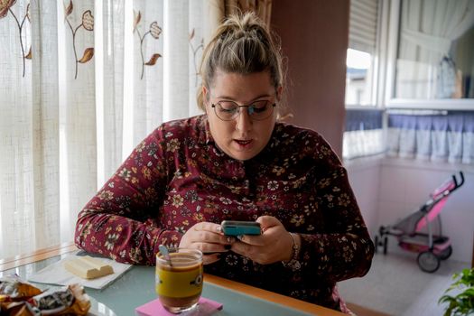 blonde woman, young with glasses, drinking coffee looking at smartphone