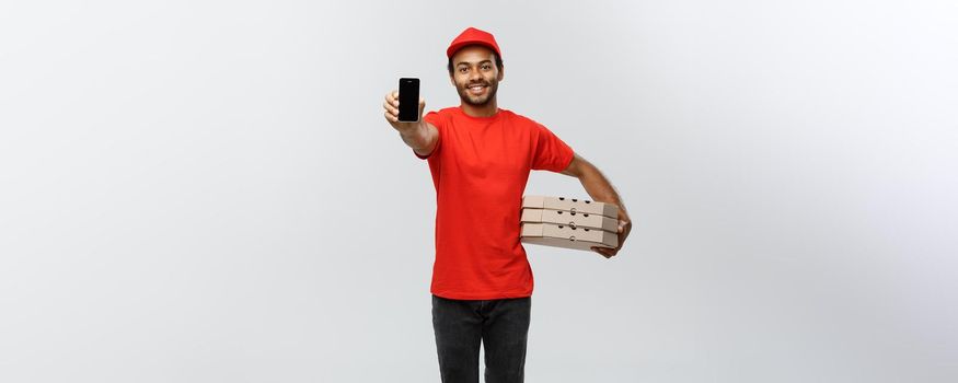 Delivery Concept - Portrait of Handsome African American delivery man or courier with pizza box showing mobile phone on you to check the order. Isolated on Grey studio Background. Copy Space