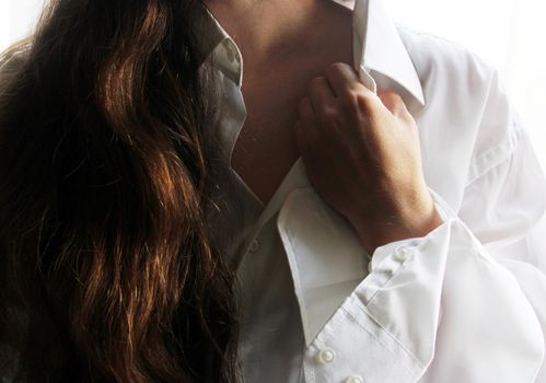 A beautiful brunette in a white shirt holds her hand to the collar of her shirt..
