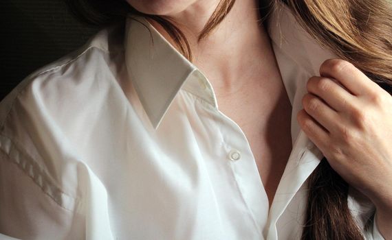 Beautiful brunette tilts her head and unbuttons the collar of a white shirt..