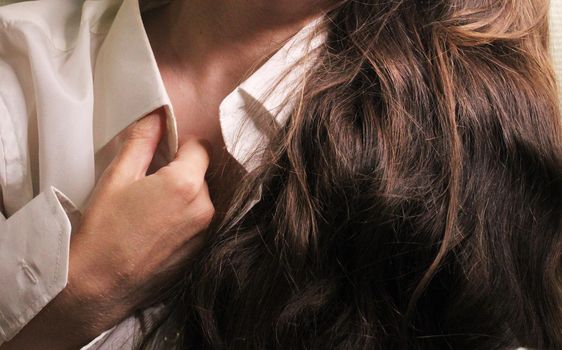 A beautiful girl with long dark hair holds her hand to the collar of a white shirt..