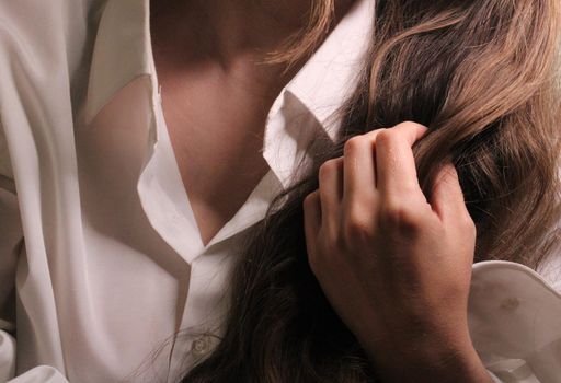 A beautiful girl in a white shirt holds long dark hair with her hand..