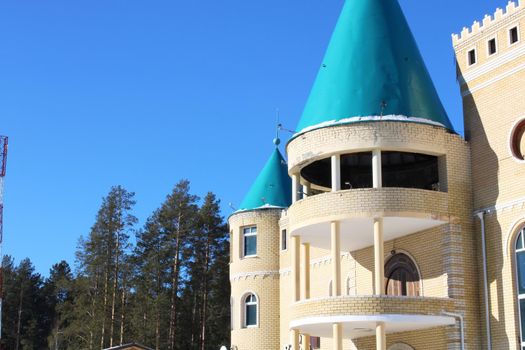 House with towers in the style of a castle of light stone against the background of the forest and blue sky..