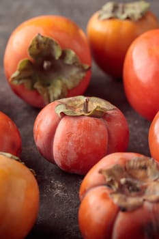 Different fresh persimmons on a dark background