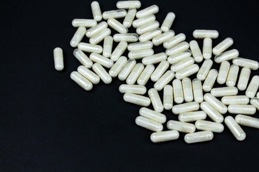 Heap of white medication and pills, capsules on black background. Top view, flat lay. Close-up.