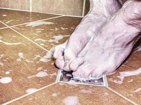 Couple of naked feet in shower. Detailed foot toes, floor tilles, stainless sink. Feet washing in bathroom with shampoo foam.