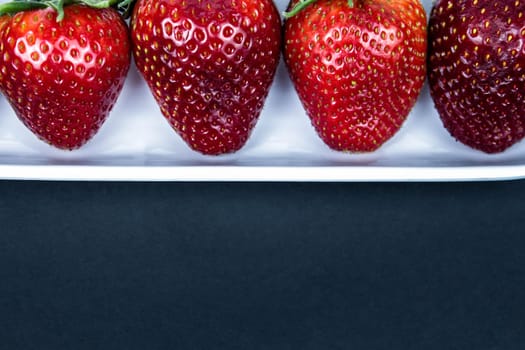 Strawberry in a white plate close up on a black background. Fresh red strawberry in white bowl on black background. side view, copy space, close up.