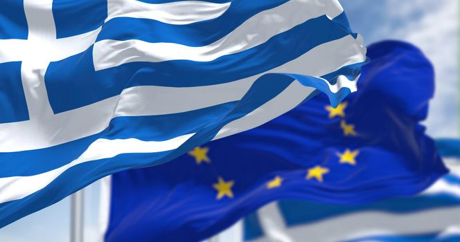 Detail of the national flag of Greece waving in the wind with blurred european union flag in the background on a clear day. Democracy and politics. European country. Selective focus.