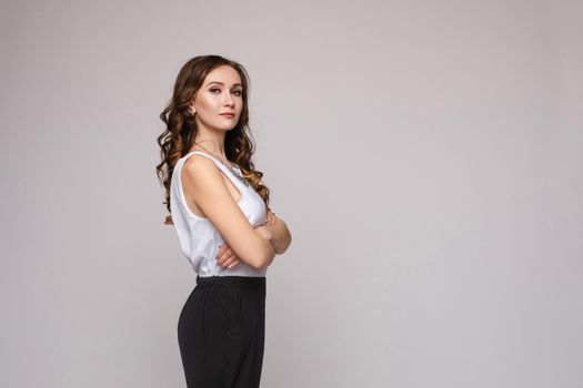 Front view of elegant successful female wearing smart outfit and glasses and posing on isolated background. Intelligent woman with folded arms looking at camera in studio. Concept of job and business.