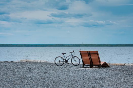 Retro styled photo of bicycle near bench on beach. Horizontal sea lane