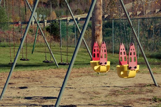 Bright yellow and red chain swings on kids playground. Autumn leaves. Covid restrictions.