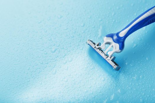 Razor blades on a blue background with drops of icy water close-up free space. The concept of purity and freshness