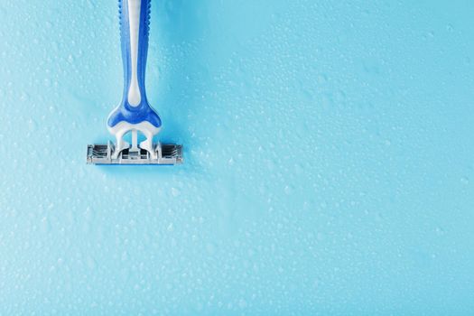 Razor blades on a blue background with drops of icy water close-up free space. The concept of purity and freshness