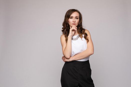 Front view of elegant successful female wearing smart outfit and glasses and posing on isolated background. Intelligent woman with folded arms looking at camera in studio. Concept of job and business.