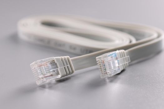 Close-up of white internet connectors placed on grey surface, cable with plastic clip at tip. Internet and telecommunications, modern technology concept