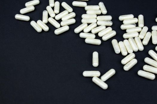 Heap of white medication and pills, capsules on black background. Top view, flat lay. Close-up.