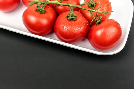 Red tomatoes on white plate on black background. Fresh tomatoes
