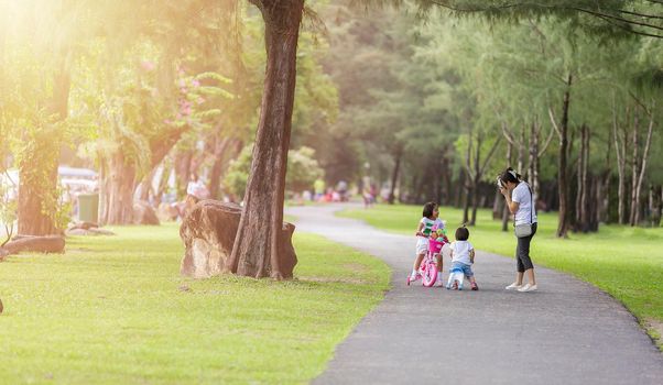 Family in park concept. Mother and her daughter play at park together. Mother shot her daugther with camera. Little girls relax with little bicycle on road in park.
Happy young mother shot picture her daugther.