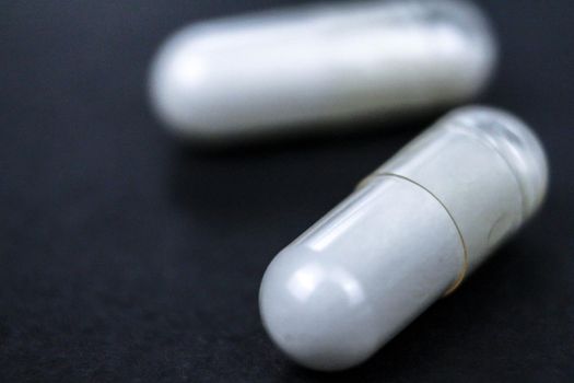 Macro view of white medication and pills, capsules on black background. Top view, flat lay. Close-up.