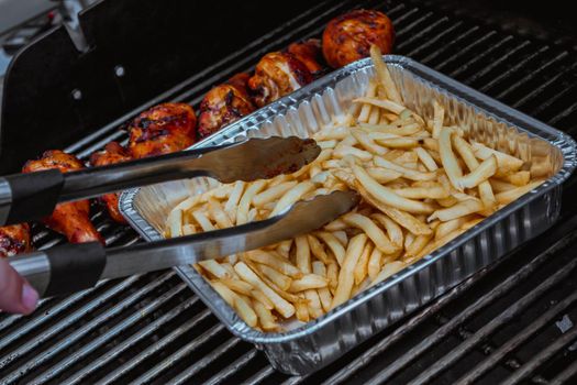 Grilled chicken on barbeque grill, delicious meat cooked on wooden charcoals with smoke. Fried potato. Fries on a foil pan