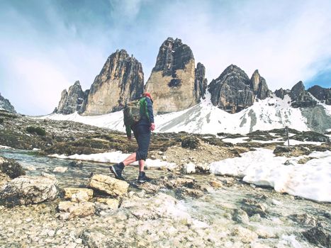 Hiker man with backpack crossing stream on stones in Dolomiti mountains. Hiking and leisure theme