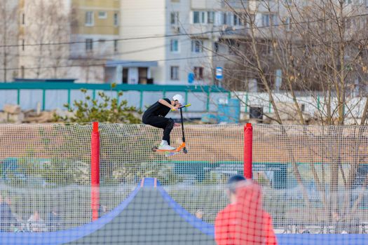 A young guy rides a stunt scooter on a skatepark ramp. Russia, Zelenograd, April 23, 2022.