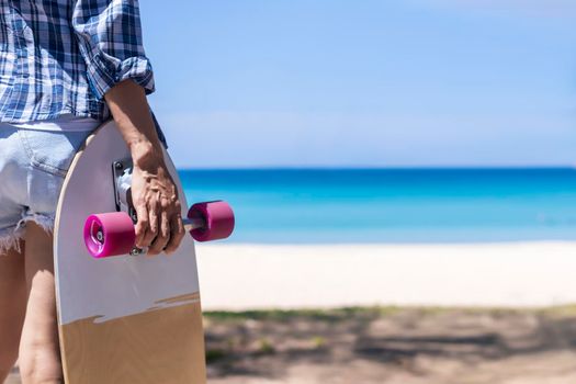 Hand of young women hold surf skate board with beach background. Women stand with surf skate relax and enjoy with tropical beach with copy space