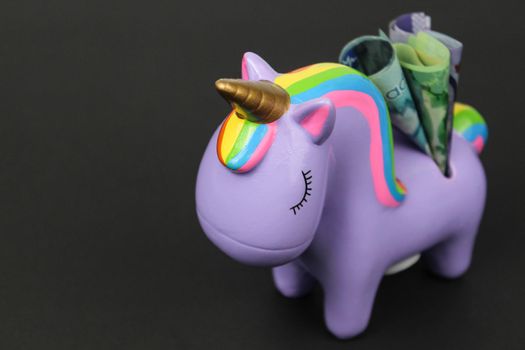 A close up profile of a piggy bank with Canadian bank notes Dollars. Unicorn bank with money on black background.