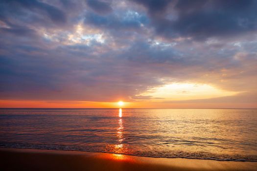 Beautiful sunset over the clam sea with cloud sky background. Sunset over tropical beach. Nature summer  concept. Peak sunset over sea with yellow light reflect on sea water. Tranquil seascape. Horizon over the water.