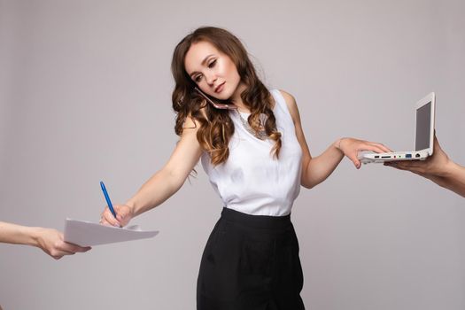 Side view of busy businesswoman talking by phone, using computer and signing papers in studio. Serious blonde looking at camera and working on isolated background. Concept of job and success.