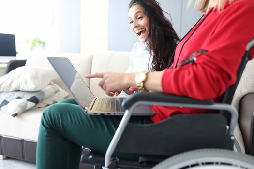 Portrait of friends spend time at home, watching movie and laughing, woman in wheelchair with laptop on lap. Disabled people, sisterhood, pastime concept