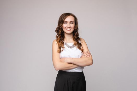 Front view of elegant successful female wearing smart outfit and glasses and posing on isolated background. Intelligent woman with folded arms looking at camera in studio. Concept of job and business.