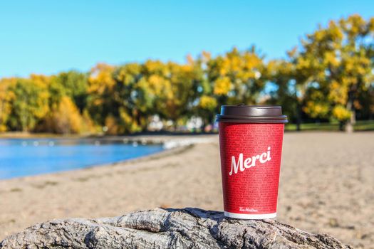 Red Paper Tim Hortons cup of coffee with Merci word on natural morning background. Fresh morning