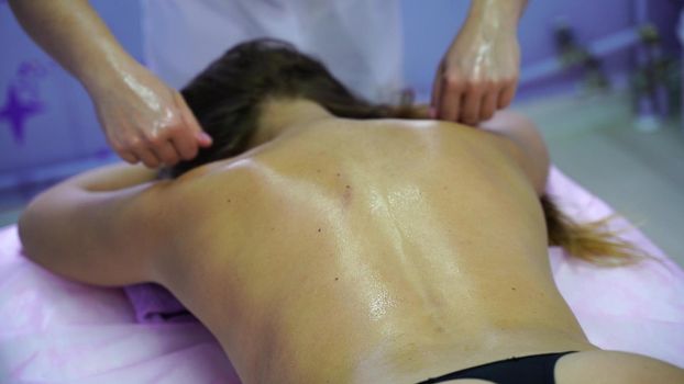 Young unrecognizable woman gets professional back massage in spa salon. Beautiful naked lady with perfect skin gets relaxing massage. Concept of luxury professional massage.