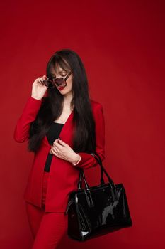 Portrait of young beautiful woman thoughtfully looking down. Brunette model in elegant costume posing at camera . Pretty lady in red sunglasses leaning one hand on other and holding it near face.